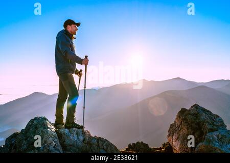 Wanderer Mann stehend mit Wanderstöcken auf einer Klippe Kante und Blick auf Tatra Berge Tal mit Wolken bedeckt. Erfolgreicher Velky Rozsutec 1610m Summ Stockfoto