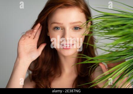 Rothaarige Junge Frau, Die Mit Grünen Pflanzenblättern Posiert, Grauer Hintergrund Stockfoto