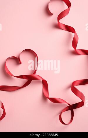 Herzförmige rote Schleife auf rosa Hintergrund. Liebe, Romantik Konzept. Vorlage für Grußkarten zum Valentinstag oder Muttertag. Stockfoto