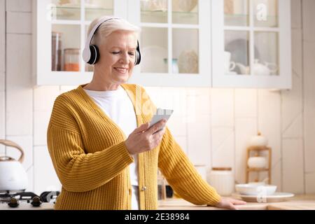 Glückliche ältere Frau, die zu Hause Musik auf dem Smartphone hört Stockfoto