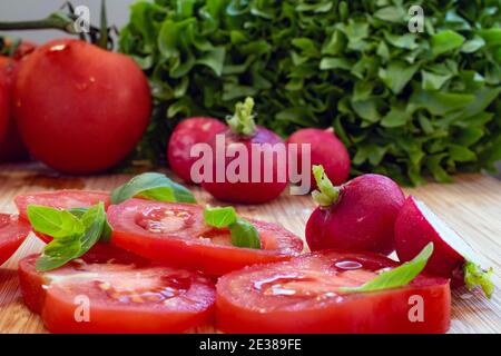 In Scheiben geschnittene Tomaten gewürzt mit frischen Basilikumblättern angeordnet unter anderem Frische Salatzutaten wie Rettich und Salat Stockfoto