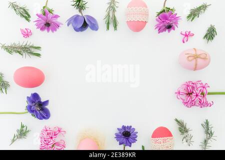 Ester Rahmenkomposition mit bunten Eiern, Frühlingsblumen, Hypericum und Lavendelblättern auf weißem Hintergrund. Flach liegend, Draufsicht Stockfoto