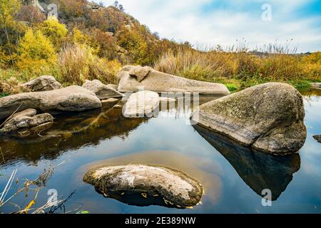 Ein schneller, flacher, sauberer Bach fließt zwischen glatten nassen großen Steinen, umgeben von hohen trockenen Klumpen, die im Wind im malerischen Ukraine schwanken Stockfoto