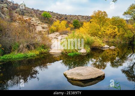 Ein schneller, flacher, sauberer Bach fließt zwischen glatten nassen großen Steinen, umgeben von hohen trockenen Klumpen, die im Wind im malerischen Ukraine schwanken Stockfoto