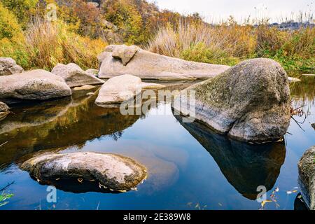 Ein schneller, flacher, sauberer Bach fließt zwischen glatten nassen großen Steinen, umgeben von hohen trockenen Klumpen, die im Wind im malerischen Ukraine schwanken Stockfoto