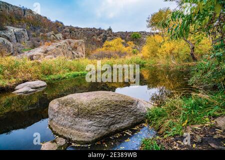 Ein schneller, flacher, sauberer Bach fließt zwischen glatten nassen großen Steinen, umgeben von hohen trockenen Klumpen, die im Wind im malerischen Ukraine schwanken Stockfoto