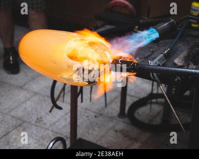 Handwerkliche Hände arbeiten mit heißem formbarem Glas und heizen es mit Gasbrenner. Nahaufnahme der Methode des Künstlers. Tschechische handgemachte Glas Studio. Stockfoto