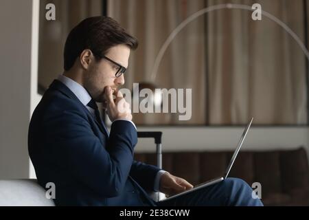 Seitenansicht nachdenklicher Geschäftsmann trägt eine Brille, die das Kinn berührt, mit einem Laptop Stockfoto
