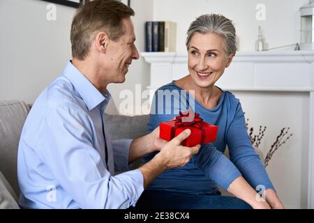 Glücklicher alter Mann gibt rote Geschenkbox an Frau macht Geschenk am Valentinstag. Stockfoto