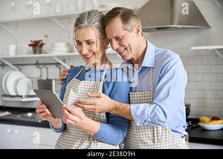 Glücklich altes Paar mit Tablet tun Lebensmittel einkaufen online zu Hause in der Küche. Stockfoto