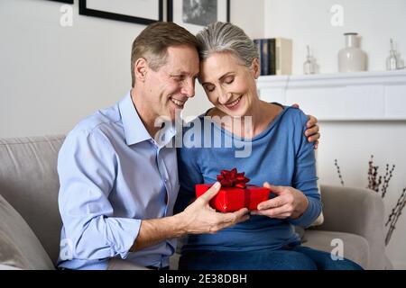 Glücklicher alter Mann gibt rote Geschenkbox an Frau macht Geschenk am Valentinstag. Stockfoto
