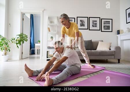 Fit aktive reife Frau hilft älteren Ehemann dabei Stretching-Übung zu Hause. Stockfoto