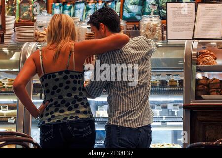 Eine Rückansicht eines jungen Paares in einem Café, das durch die Glastheke die Restaurants ansieht. Stockfoto