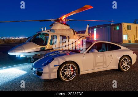 Ein Agusta 109 Power Executive Hubschrauber bei Dämmerung neben einem Porsche 911 Auto. Stockfoto