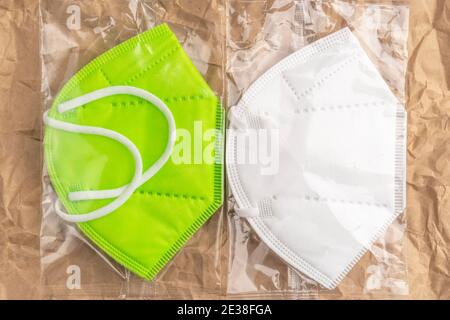 KN95 Schutzmasken in glänzender Kunststoffverpackung auf zerknittert faltenem Papierhintergrund Nahaufnahme. Grün und weiß. Stockfoto