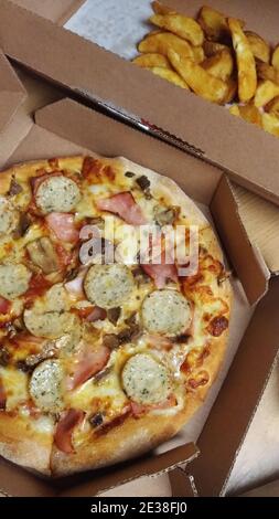 Pizza mit Schinken, Weißwürsten und Bratkartoffeln in Pappkartons Stockfoto