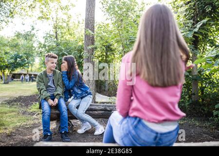 Junge und ein Mädchen klatschen über ein Mädchen, das in ihrer Nähe sitzt. Mädchen flüstert etwas zu jungen Ohr und Spaß zusammen. Selektiver Fokus. Stockfoto
