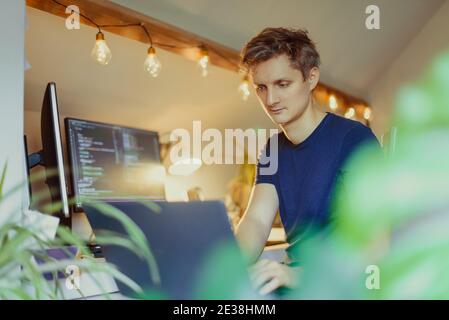 Ein Mann, der an einem Schreibtisch sitzt und von zu Hause aus an seinem Computer arbeitet. IT-Spezialist Programmierer schreiben Code auf seinem pc und Laptop. Entwickler Remote Home Office Stockfoto