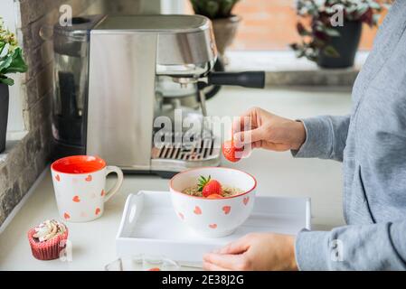 Frau Hinzufügen von Erdbeerfrüchten zu Haferbrei Haferbrei Schüssel. Vorbereitung Überraschungsfrühstück für Liebhaber am Valentinstag. Einfache festliche gesunde Ernährung Idee Stockfoto