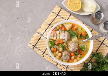 Türkische Suppe mit Kichererbsen, Fleischbällchen und Gemüse in einer weißen Schüssel auf grauem Hintergrund. Mit Ort für Text. Stockfoto