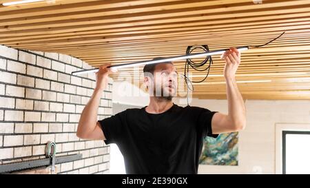 Ein Elektroinstallateur installiert die elektrische Verkabelung im Haus. Die Mietsaugdecke wechselt die Beleuchtung an der stilvollen Holzdielen-Decke. Ein Baumeister ist Stockfoto