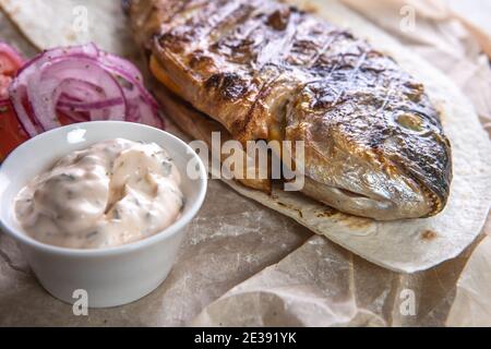 Gegrillter dorado-Fisch mit Sauce, Gurken, Tomaten und Zwiebeln auf einem Holztablett Stockfoto