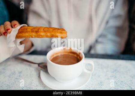 Nahaufnahme einer Person, die einen Churro in heiße Schokolade taucht. Selektiver Fokus Stockfoto