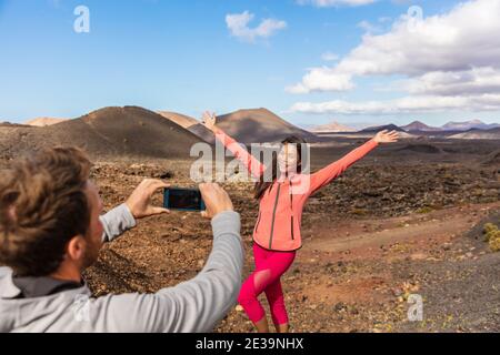 Touristen, die Fotos machen, die draußen auf Europa reisen, Mädchen posieren für Freund mit den Armen nach oben Spaß auf Timanfaya Nationalpark, Lanzarote Stockfoto