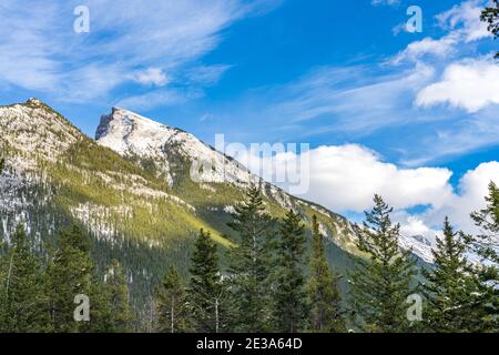 Schneebedeckte Bergkette Mount Rundle mit verschneiten Wald über blauem Himmel und weißen Wolken im Winter sonnigen Tag. Banff National Park, Canadian Rockies. Stockfoto