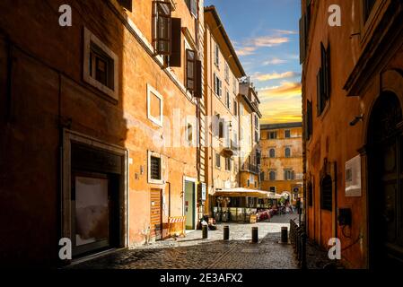 Eine schmale Gasse im historischen Zentrum von Rom, Italien, führt zu einem kleinen Bürgersteig-Café bei Sonnenuntergang. Stockfoto