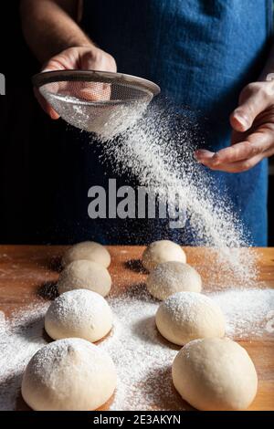 Baker's Hände streuen Teig mit Mehl mit einem Sieb Stockfoto