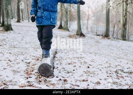 Junge geht auf einem Log. Handausgleich. Winterlandschaft im Wald. Aktivitäten im Winterwald. Weihnachtsfeiertage. Interessante Spiele im Winter Stockfoto