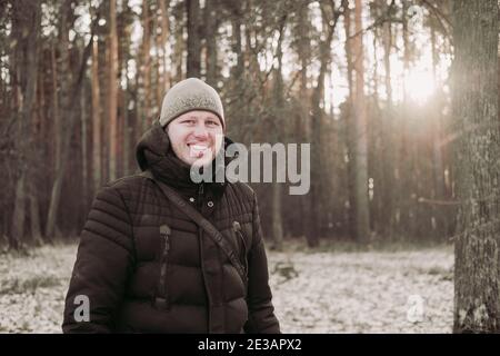 Lächelnder Mann im Winterwald. Glücklicher Mann geht im verschneiten Wald. Ein Mann mit guter Laune. Wanderung durch den Winterwald. Reisen im Winter. Naturwal Stockfoto