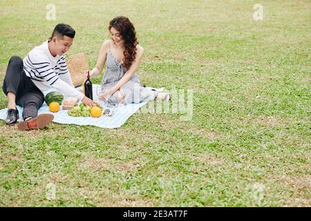 Glückliches junges Paar genießt romantisches Picknick im Stadtpark, Wein trinken und Obst essen Stockfoto