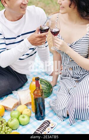Zugeschnittenes Bild von lächelnden jungen asiatischen paar Toasten mit Brille Rotwein bei einem romantischen Picknick am Valentinstag Stockfoto