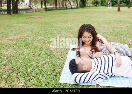 Junge asiatische Paar in Liebe reden, wenn auf Decke liegen Im Stadtpark Stockfoto