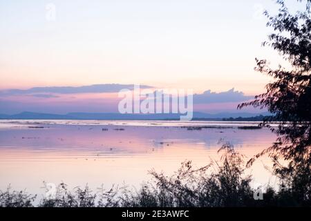Lange Belichtung Vanille bunten Himmel und See Reflexion mit Bergen im Hintergrund. Verschwommenes wildes Gras weht im Wind im Vordergrund Stockfoto