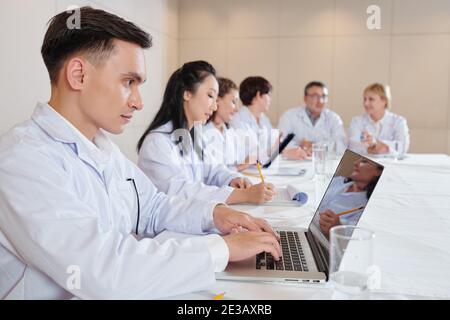 Ernsthafte junge Forscher arbeiten auf Laptop, wenn die Teilnahme an Treffen mit Wissenschaftler widmen sich neuen Coronavirus-Impfstofftests Stockfoto