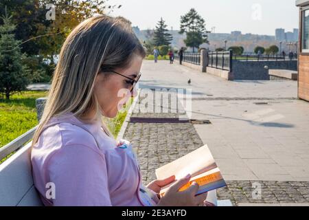 Junge Frau liest auf einer Bank am Ufer des Irkut Flusses in Irkutsk. Stockfoto