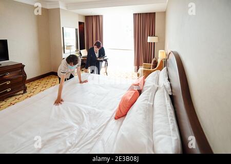 Hotelmanager mit digitalem Tablet und erklärt dem neuen Zimmermädchen, wie es geht Machen Sie das Bett richtig Stockfoto