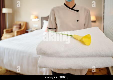 Beschnittenes Bild von jungen weiblichen Hotelmädchen, die in der Suite stehen Mit Stapel frischer Handtücher und Calla Lily Stockfoto