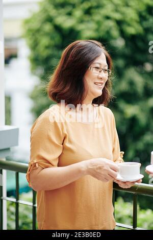 Positive ziemlich reife vietnamesische Frau im Freien und Trinkbecher stehen Des Morgentees Stockfoto