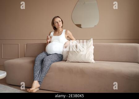 Schwangere Frau trinkt Wasser im Wohnzimmer Stockfoto