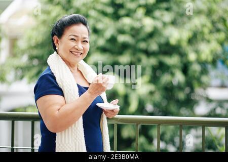 Glückliche ältere vietnamesische Frau im Freien stehen und trinken Tasse Kaffee am Morgen Stockfoto