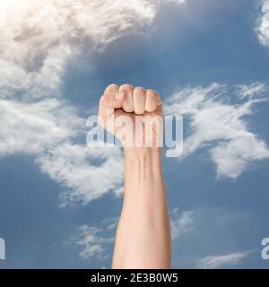 Geballte Faust in der Luft.männliche Hand hebt geballte Faust der Solidarität. Protestant hält die erste Hand über bue Himmel. Hand steigt bis zum Himmel.Mann Klenche Stockfoto