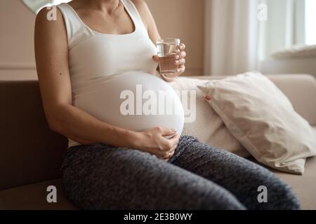 Schwangere Frau trinkt Wasser im Wohnzimmer Stockfoto