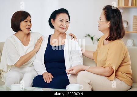 Fröhliche asiatische ältere Frauen wünschen ihrer Freundin alles gute zum Geburtstag Und sie auf die Schulter klopfend Stockfoto