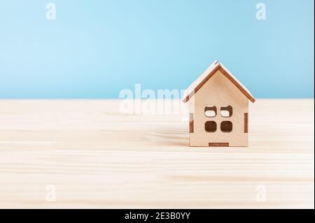 Kleines Holzmodellhaus auf Holztisch. Mini Wohn-Handwerk Haus auf blauem Hintergrund. Kleines Hausmodell. Familienleben und Geschäftsimmobilien, insur Stockfoto