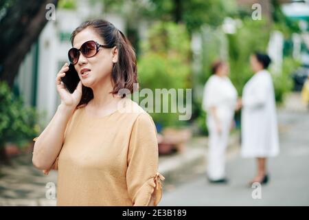 Porträt von älteren Frau in Sonnenbrille zu Fuß im Park und Anruf am Telefon Stockfoto