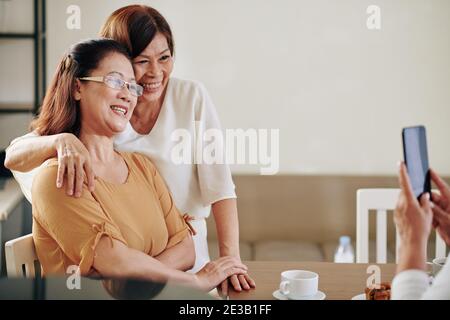 Glückliche ältere vietnamesische Freundinnen umarmen und posieren für Foto Auf dem Smartphone Stockfoto